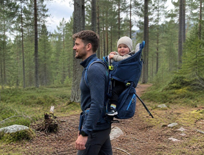 Far bærer et lite barn i en mørkeblå Deuter Kid Comfort bæremeis på en norsk fjellsti.