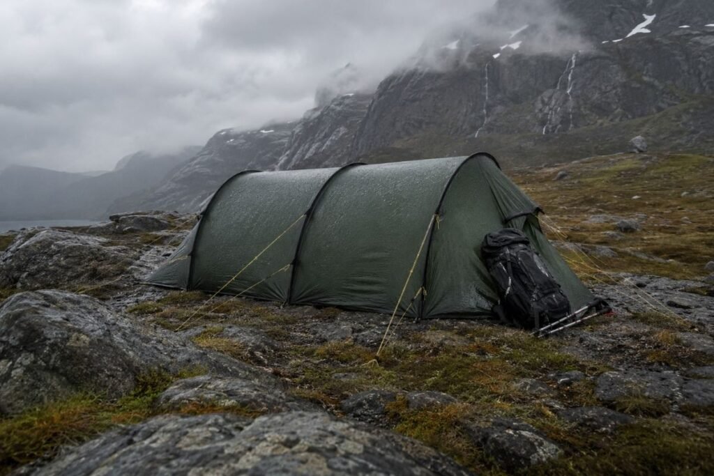 Tunneltelt satt opp med stramme barduner i regn og vind på et åpent norsk fjellområde.